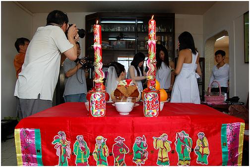 Dos velas grandes encendidas en la mesa de ofrendas durante la ceremonia para el matrimonio en casa. La tela de la mesa está decorada con los dibujos de los “Ocho Inmortales”. (kodomut/Flickr)